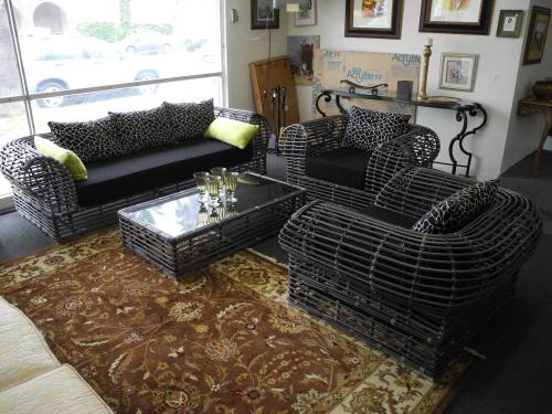 A cozy living room setup featuring black wicker furniture with patterned cushions and a glass coffee table on a decorative rug.