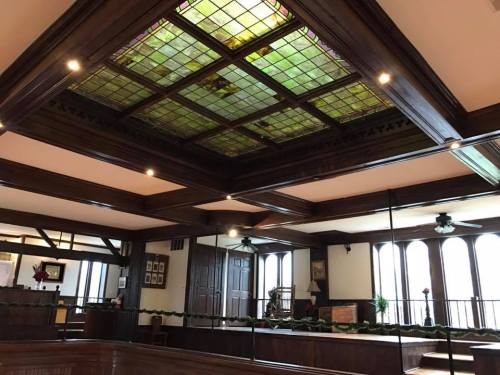 Interior view of a room featuring a stained glass ceiling, wooden beams, and large windows with decorative elements.