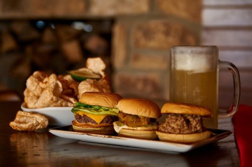 Three delicious burgers on a plate, accompanied by a bowl of pork rinds and a frosty mug of beer.