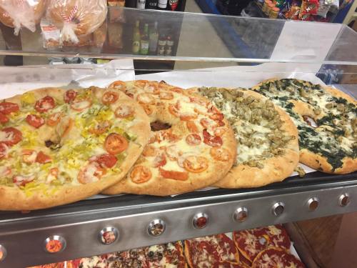 Four types of pizza on a display, featuring toppings like tomatoes, onions, spinach, and yellow peppers.