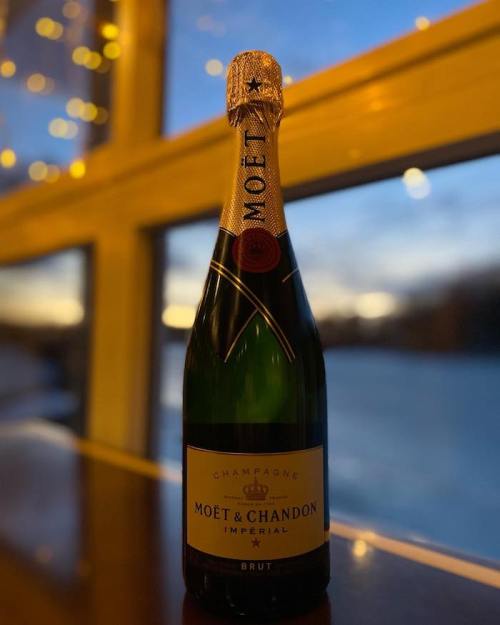 A bottle of Moët & Chandon Imperial Brut champagne sits on a table with a scenic background at sunset.