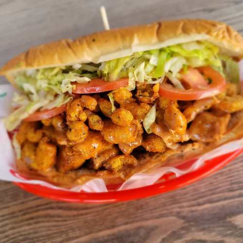 A loaded sandwich with fried shrimp, lettuce, and tomato, served in a toasted bun on a red tray.