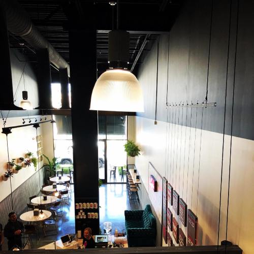 A modern café interior with a large pendant light, green seating, and tables, featuring plants and a welcoming atmosphere.