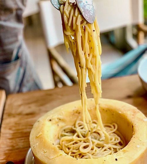 A fork lifts spaghetti from a cheese wheel, showcasing creamy pasta being served.