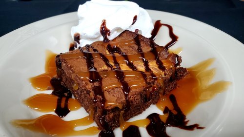 A rich chocolate dessert topped with whipped cream and drizzled with chocolate and caramel sauces on a plate.