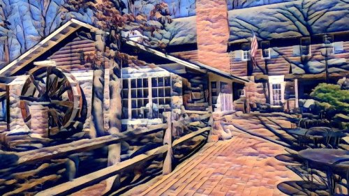 A rustic building with a stone chimney, surrounded by trees and a patio, featuring a large wheel and an American flag.