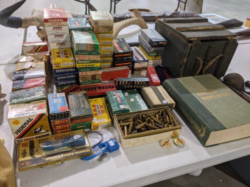 A table displaying various ammunition boxes, a vintage book, and other related items in a spacious setting.