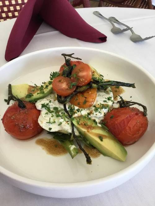 A plate of fresh salad with avocado, roasted tomatoes, and herbs, garnished with a drizzle of sauce.