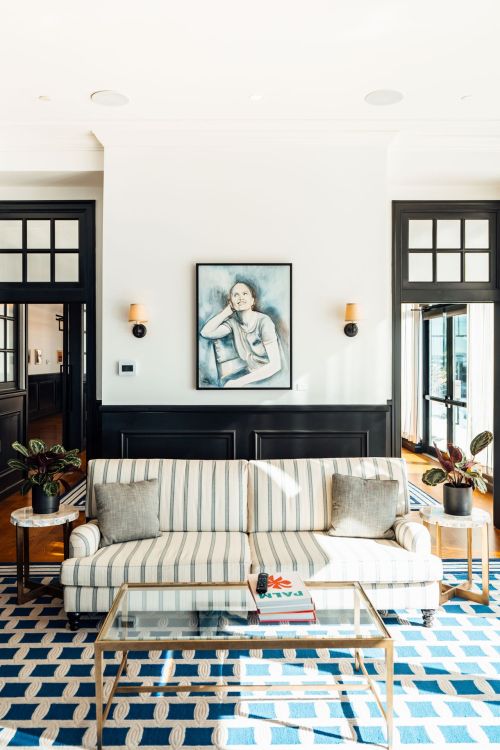 Bright living room with a striped sofa, glass coffee table, and a large artwork on the wall, featuring plants and natural light.