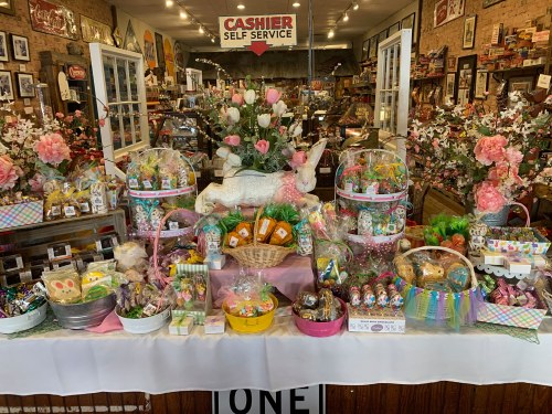 A colorful display of Easter baskets and treats, featuring a decorative bunny and floral arrangements in a shop setting.