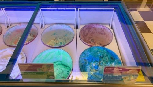 A display of ice cream tubs with various flavors, some nearly empty, in a colorful ice cream shop.