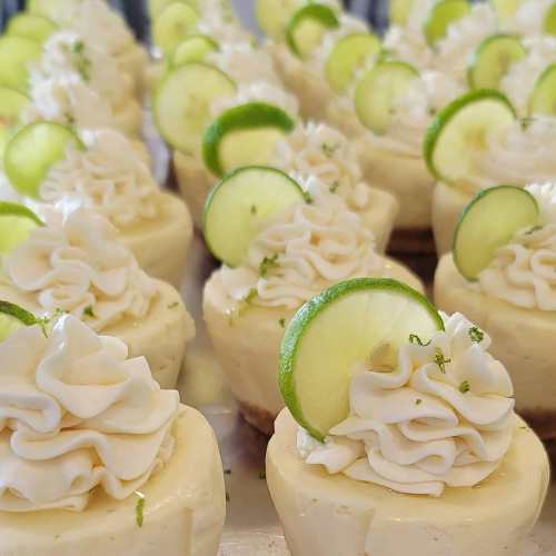 A close-up of mini lime cheesecakes topped with whipped cream and lime slices, arranged in a neat row.