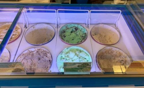 A display of various ice cream flavors in a freezer, featuring green mint, white vanilla, and other assorted flavors.