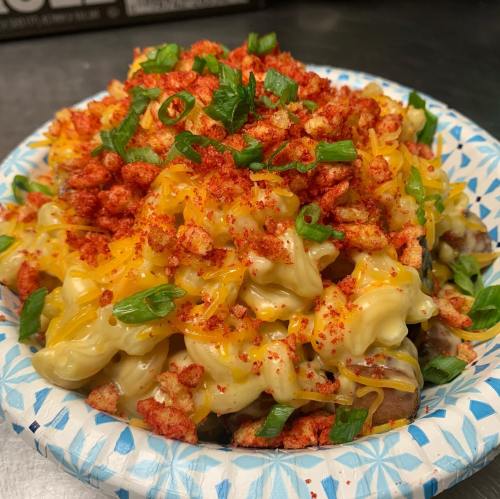 A bowl of creamy macaroni topped with cheese, crushed snacks, and green onions.