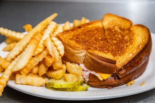 A grilled cheese sandwich with crispy fries and a pickle slice on a white plate.
