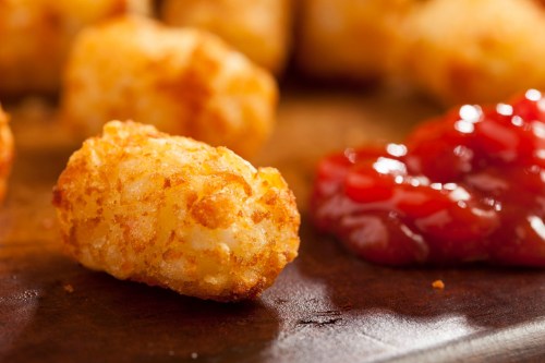 Crispy golden tater tots served with a side of ketchup on a wooden surface.