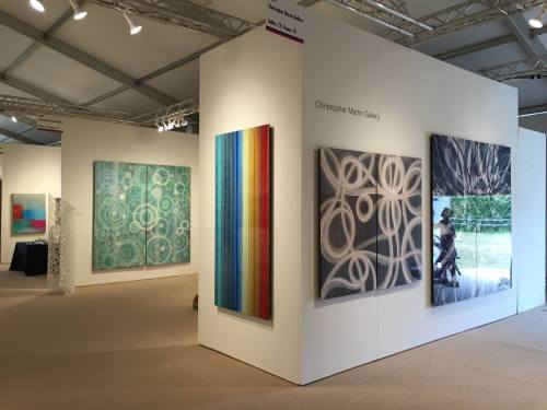 Art gallery interior featuring colorful abstract paintings and a photograph on display. Bright, spacious atmosphere.