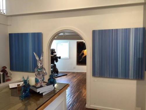 Art gallery interior featuring blue striped paintings, a glass bunny sculpture, and a sculpture in the background.