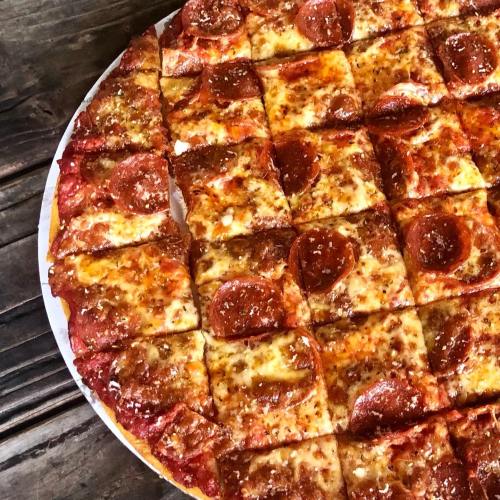 A close-up of a pepperoni pizza, sliced into squares, with melted cheese and a crispy crust on a wooden table.
