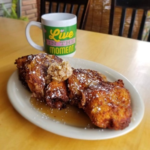 A plate of French toast topped with syrup and a dollop of butter, next to a colorful mug that says "Live in the Moment."