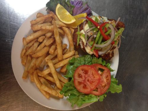 A plate with crispy fries, a burger topped with lettuce, tomato, onions, and peppers, garnished with a lemon wedge.
