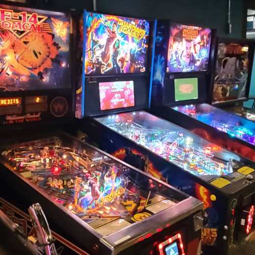 Three colorful pinball machines featuring "F-14 Tomcat" and "Guardians of the Galaxy" in a dimly lit arcade.