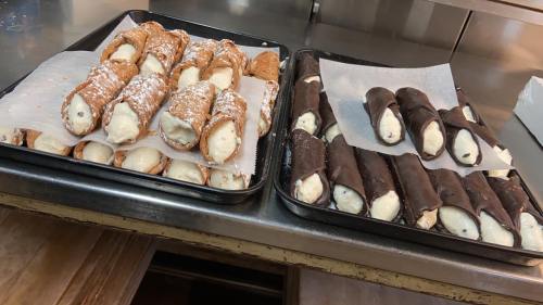 Two trays of cannoli: one filled with ricotta cream and dusted with powdered sugar, the other coated in chocolate.