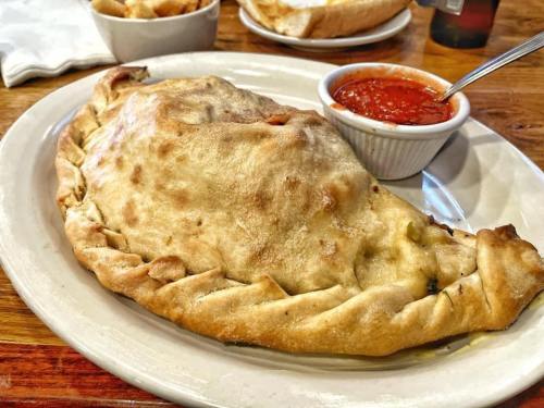 A golden-brown calzone on a plate, served with a small bowl of marinara sauce.
