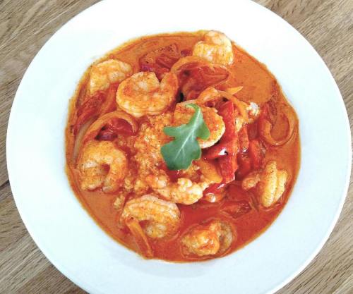 A bowl of shrimp in a creamy red sauce with peppers and onions, garnished with a green leaf.