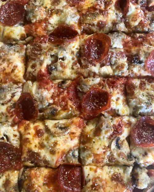 A close-up of a rectangular pizza topped with melted cheese, pepperoni, and mushrooms.