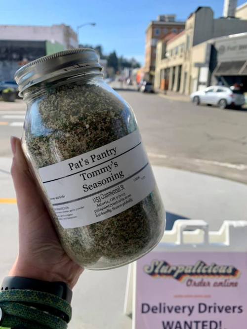 A hand holds a jar of "Tommy's Seasoning" from Pat's Pantry, with a street view in the background.