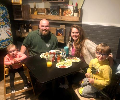 A family of four enjoys a meal together at a table, with two children in high chairs and smiling adults.