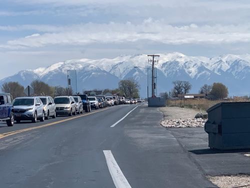 A long line of cars on a road with snow-capped mountains in the background under a cloudy sky.