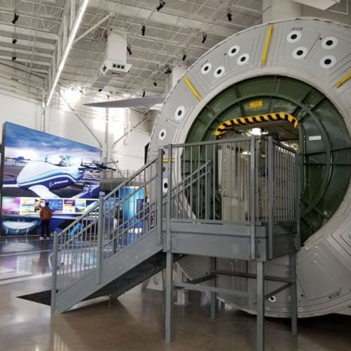 A large circular structure resembling a spacecraft, with a staircase, in a modern exhibition space featuring aviation displays.