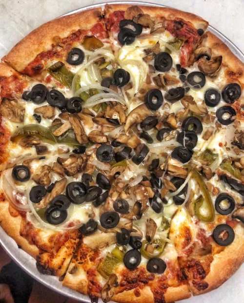 A pizza topped with mushrooms, black olives, green peppers, and onions on a golden crust.