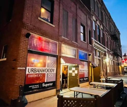 Exterior of Urbanwoody Brewery at dusk, featuring a brick building and outdoor seating.
