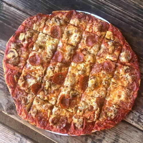 A round pizza topped with pepperoni, sausage, mushrooms, and melted cheese, cut into square slices on a wooden table.