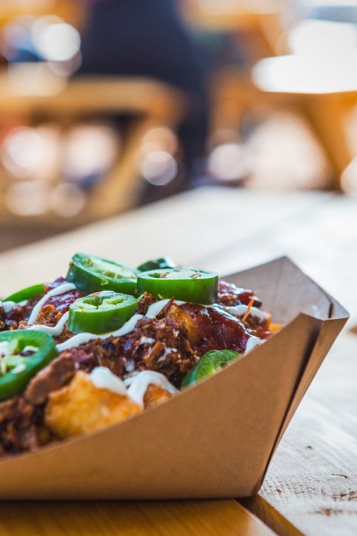 A close-up of a tray of nachos topped with jalapeños, sour cream, and a savory meat mixture on a wooden table.