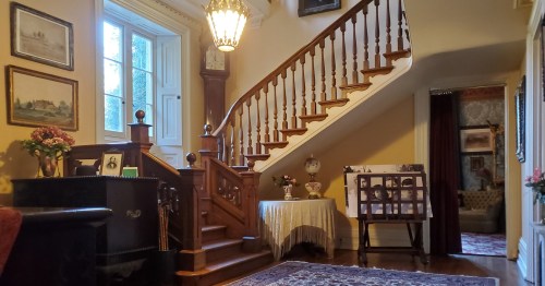 A cozy foyer with a wooden staircase, vintage decor, and a chandelier, leading to a warmly lit living area.