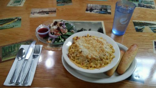 A bowl of baked macaroni and cheese with two breadsticks, a side salad, and a glass of water on a wooden table.
