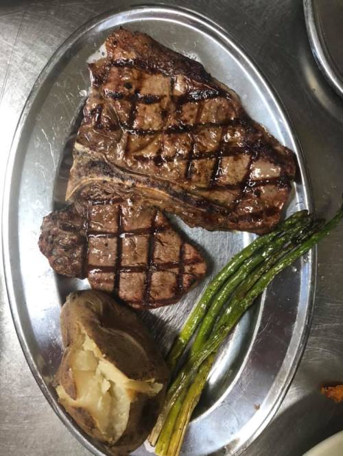 A silver platter with grilled steak, asparagus, and a baked potato.