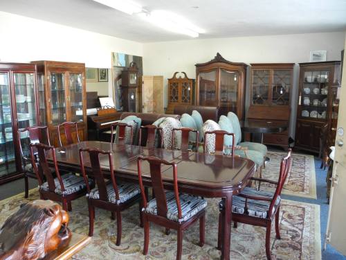 A spacious room filled with wooden furniture, including a large dining table, chairs, and display cabinets.