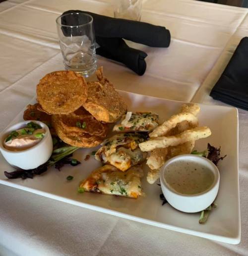 A plate of assorted appetizers including crispy snacks, dips, and garnishes on a white tablecloth.