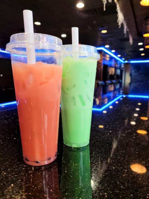 Two colorful drinks in clear cups with straws, one pink and one green, sitting on a glossy black countertop.