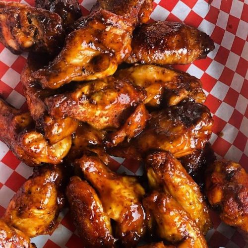 A close-up of glazed chicken wings piled in a red and white checkered basket.