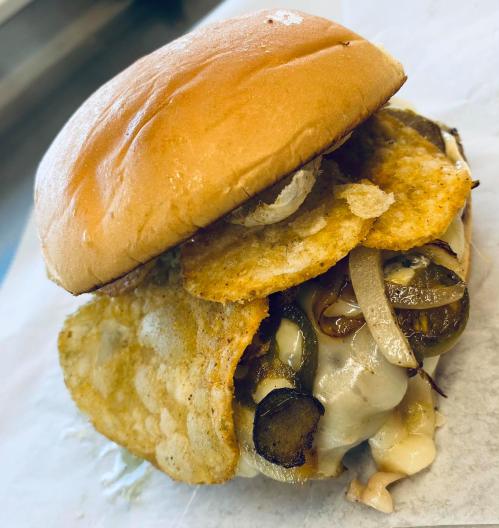 A close-up of a burger with melted cheese, pickles, onions, and crispy potato chips on a soft bun.