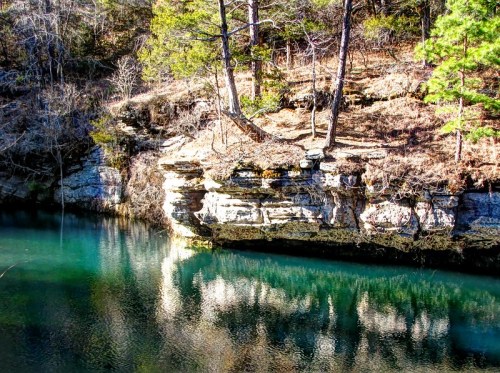 A serene river scene with rocky cliffs and trees reflecting in the clear water.