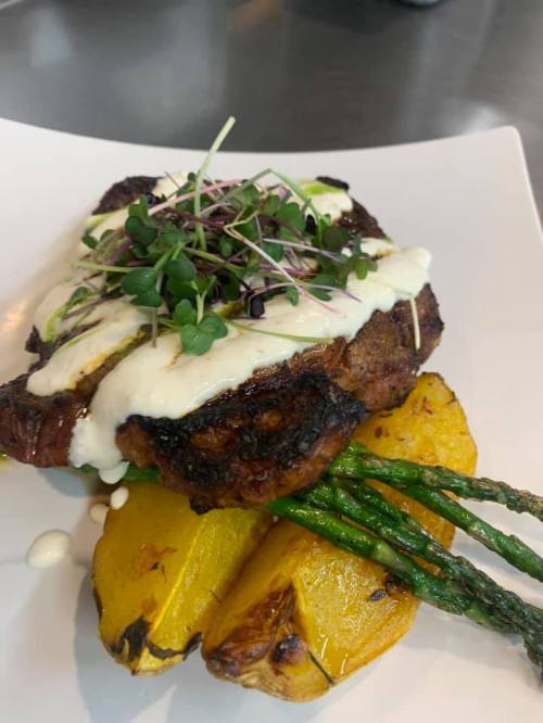 A grilled steak topped with creamy sauce, served with roasted squash and asparagus on a white plate.