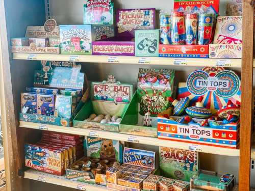 A colorful display of vintage-style toys and games on wooden shelves, including puzzles, tops, and card games.