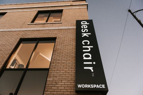 Sign for "desk chair" workspace on a brick building, with a clear evening sky in the background.